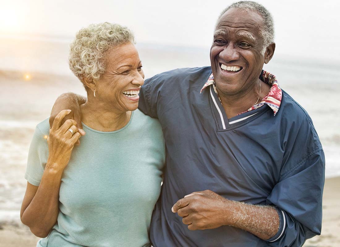 Individual Retirement Account - Senior Couple Laughing and Embracing One Another While Walking along the Beach at Sunset